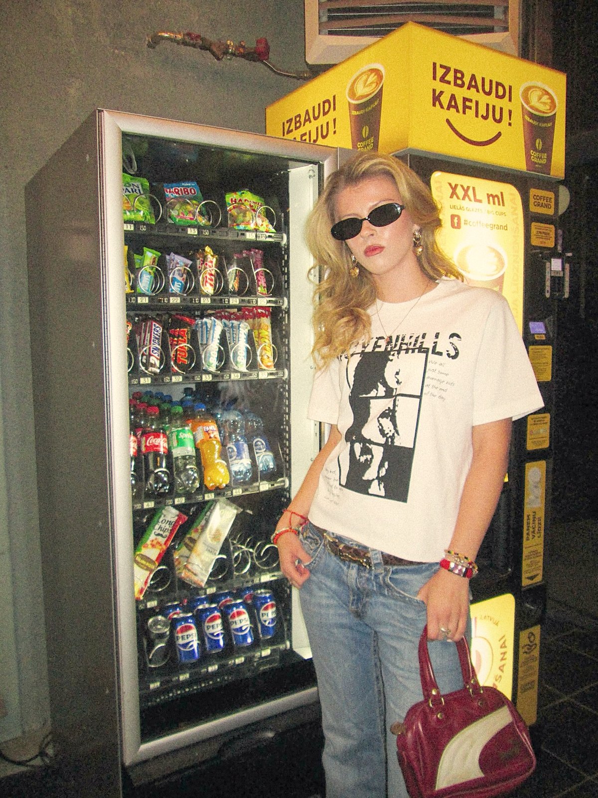 Model in sunglasses wearing the ART WILL TEE next to a lit vending machine at night
